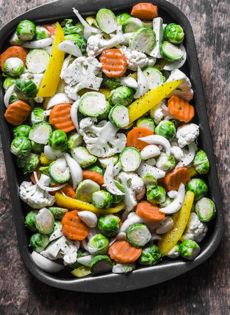 Raw ingredients for cooking vegetarian lunch - seasonal vegetables - brussels sprouts, carrots, cauliflower, pumpkin, onion, sweet pepper on a baking tray on a wooden background, top viewの写真素材