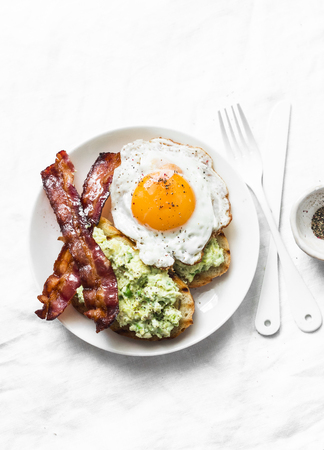 Healthy nutritious breakfast or snack - avocado toast, bacon and fried egg on light background, top viewの写真素材