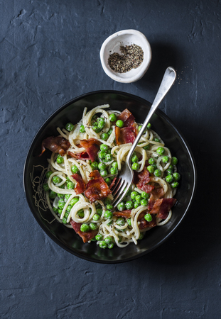 Spaghetti with bacon and creamy green peas on a dark background, top viewの写真素材