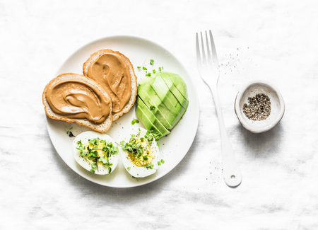 Peanut butter toasts, boiled egg with micro greens, avocado - healthy breakfast or snack on a light background, top viewの写真素材