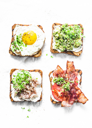 Variety of sandwiches for breakfast, snack, appetizers - avocado puree, fried egg, tomatoes, bacon, cream cheese, smoked mackerel grilled whole grain bread sandwiches. On a light background, top viewの写真素材