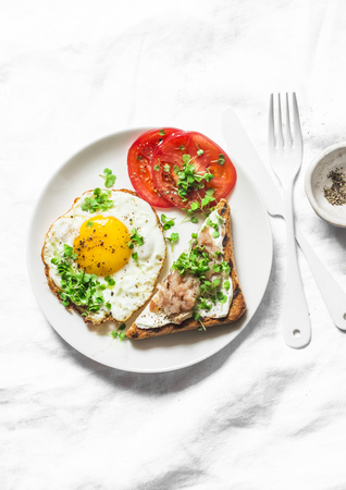 Healthy breakfast or brunch - fried egg, fresh tomatoes and smoked mackerel toast on a light background, top viewの写真素材