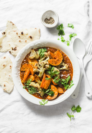 Roasted curry vegetables. Sweet potatoes, cauliflower, carrots, onions, pumpkin with curry sauce on light background, top view. Vegetarian food conceptの写真素材