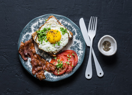 Nutritious breakfast - fried egg toast, bacon and tomatoes on a dark background, top viewの写真素材