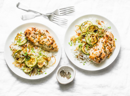 Served lunch - dijon baked chicken with rice, courgettes and fried onions on light background, top viewの写真素材