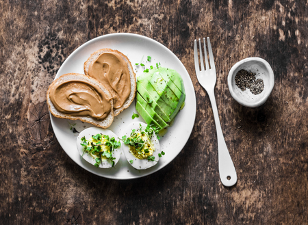 Peanut butter toasts, boiled egg with micro greens, avocado - healthy breakfast or snack on a wooden background, top viewの写真素材