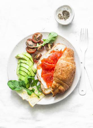 Morning breakfast table - croissant with cream cheese and smoked salmon, avocado and cherry tomatoes. Delicious balanced breakfast, brunch or snack on a light background, top viewの写真素材