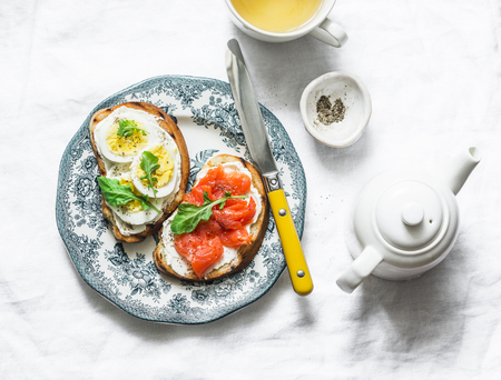 Delicious healthy breakfast or snack - sandwiches with cream cheese, boiled egg and smoked salmon on a light background, top viewの写真素材