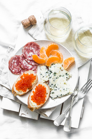 Delicious appetizer - red caviar sandwiches, blue cheese, salami, tangerines and white wine on a light background, top view. Flat layの写真素材
