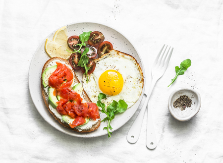 Whole grain bread, cream cheese, avocado, smoked salmon sandwich and fried egg - delicious breakfast, snack, brunch on a light background, top viewの写真素材