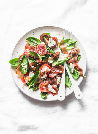 Crispy fried prosciutto, cherry tomatoes, spinach, parmesan salad on light background, top view. Copy spaceの写真素材