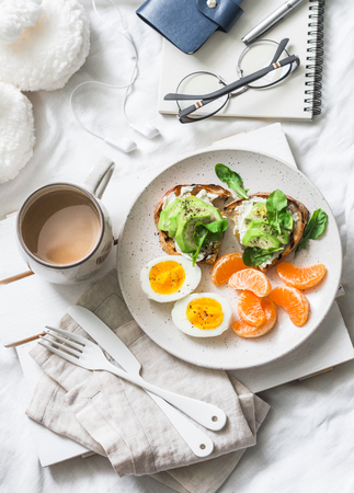 Cozy breakfast in bed still life - coffee, avocado sandwiches, boiled egg and tangerine on a light background, top view. Morning inspiration planの写真素材