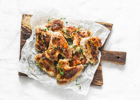 Roasted chicken wings on wooden chopping board - delicious appetizers, tapas on light background, top viewの写真素材