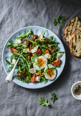 Breakfast salad - rocket, cherry tomatoes, mozzarella and boiled egg with olive oil, mustard, lemon dressing on a grey background, top viewの写真素材