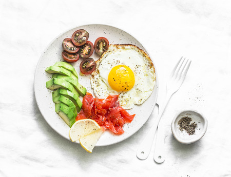 Delicious brunch - fried egg, avocado, cherry tomatoes and smoked salmon on light background, top viewの写真素材