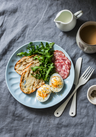 Delicious breakfast or snack - salami sausage, boiled egg, arugula, grilled bread and coffee on a gray background, top viewの写真素材