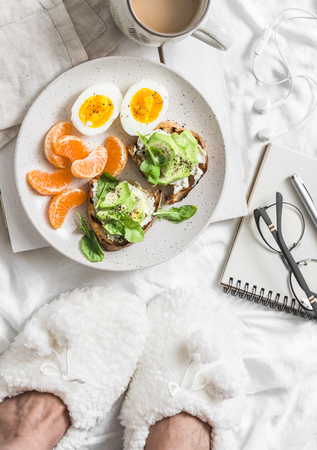 Breakfast in bed. Coffee, avocado sandwiches, boiled egg and tangerine on a light background, top view. Morning inspirationの写真素材