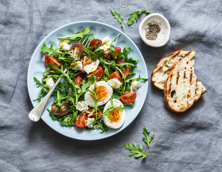 Breakfast salad - rocket, cherry tomatoes, mozzarella and boiled egg with olive oil, mustard, lemon dressing on a grey background, top viewの写真素材