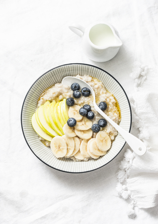 Steel-cut oats breakfast porridge with apple, banana, blueberry and honey on a light background, top view. Vegetarian healthy foodの写真素材