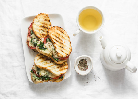 Hot grilled tomatoes, spinach, mozzarella sandwiches and green tea - healthy breakfast, snack on a light background, top viewの写真素材