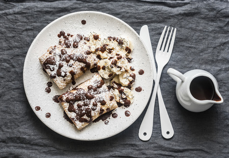 Stuffed ricotta cheese crepes with chocolate sauce, bananas and nuts on a grey background, top view. Delicious breakfast, dessertの写真素材