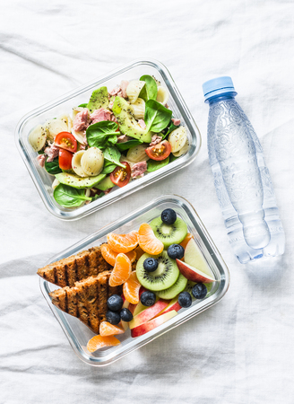 Healthy eating lifestyle concept. Office food lunch box - sweet and savory lunch, snack and clean water. Pasta, tuna, spinach, avocado salad and fruit, peanut butter sandwiches lunch box on light background, top viewの写真素材
