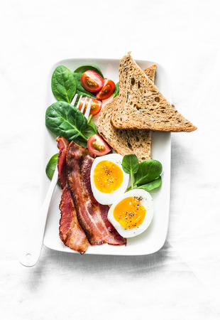 Delicious breakfast - soft boiled egg, bacon, spinach tomatoes salad on light background, top viewの写真素材