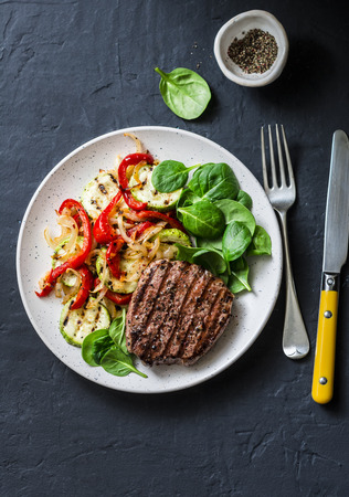 Beef steak with grilled  vegetables, sweet pepper, zucchini and fresh spinach on a dark background, top view. Delicious healthy balanced lunchの写真素材