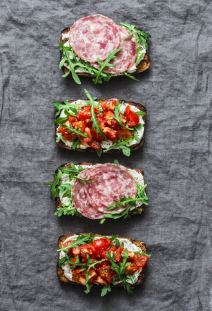 Tomatoes, italian sausage and rocket salad whole grain bread sandwiches on a gray background, top view. Copy space, flat lay. Delicious appetizers for wine, tapasの写真素材