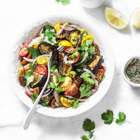 Roasted eggplant, sweet tomato and cilantro mediterranean style salad on light background, top view. Vegetarian food conceptの写真素材