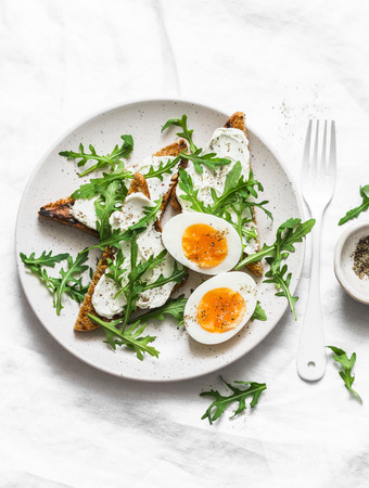Delicious breakfast, brunch or snack - cream cheese toast, arugula salad and soft boiled egg on a light background, top viewの写真素材