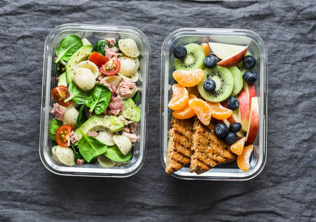 Healthy eating lifestyle concept. Office sweet and savory food lunch box. Pasta, tuna, spinach, avocado salad and fruit, peanut butter sandwiches lunch box on gray background, top viewの写真素材
