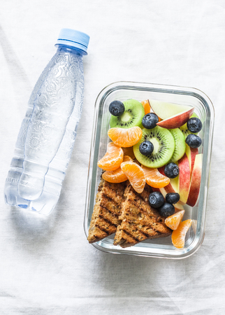 Healthy food snack sweet vitamin lunch box and bottle of clean water on a light background, top view. Peanut butter toast, apples, kiwi, tangerines, blueberry lunch boxの写真素材