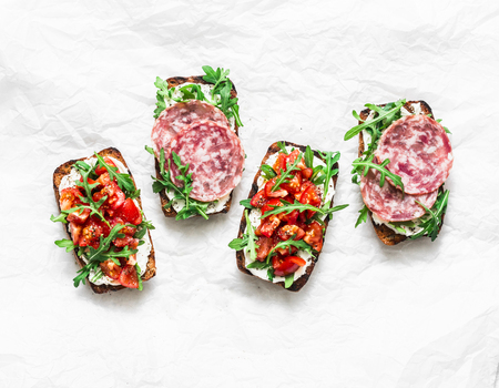Tomatoes, italian sausage and rocket salad whole grain bread bruschetta on a light background, top view. Copy space, flat lay. Delicious appetizers for wine, tapasの写真素材