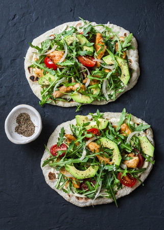 Pan-fried flatbread chicken, avocado, tomatoes, arugula pizza on dark background, top viewの写真素材
