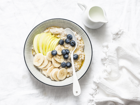 Oats breakfast coconut milk porridge with apple, banana, blueberry and honey on a light background, top view. Vegetarian healthy foodの写真素材