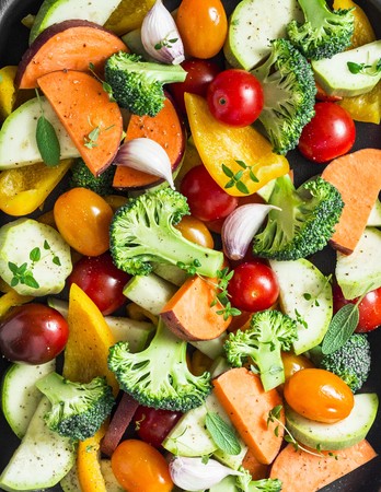 Cut seasonal raw vegetables - sweet potatoes, broccoli, bell peppers, zucchini, tomatoes, onions, garlic with spices and herbs. Ingredients to prepare vegetable side dish. Healthy vegetarian food concept. Vegetables backgroundの写真素材