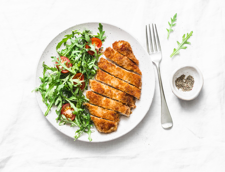 Traditional chicken schnitzel with arugula cherry tomatoes salad on light background, top viewの写真素材