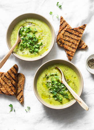 Mashed spring vegetable soup served with micro greens and whole grain crackers on a light background, top view. Healthy vegetarian food conceptの写真素材