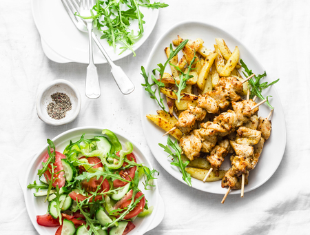 Greek soulvaki with fried potatoes and tomatoes, cucumbers, pepper, arugula salad on a light background, top viewの写真素材