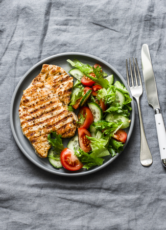 Grilled turkey chops and tomatoes, cucumbers, greens salad on a gray background, top view. Healthy food diet conceptの写真素材