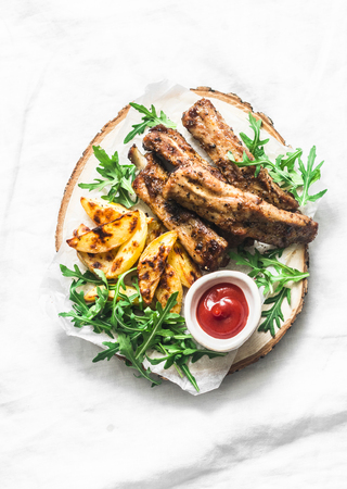 Grilled pork ribs and french fries on wooden board on light background top view. Delicious lunch, appetizers, tapasの写真素材