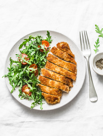 Traditional chicken schnitzel with arugula cherry tomatoes salad on light background, top viewの写真素材