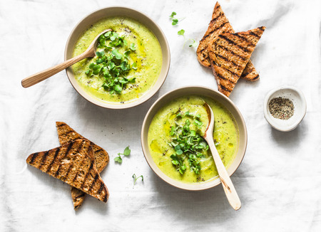 Mashed spring vegetable soup served with micro greens and whole grain crackers on a light background, top view. Healthy vegetarian food conceptの写真素材
