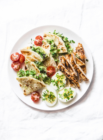 Grilled chicken, avocado cream cheese quesadilla, boiled eggs, vegetables - delicious snack, appetizer, tapas on a light background, top viewの写真素材