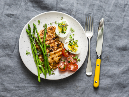Grilled chicken steak, asparagus, boiled egg, cherry tomatoes - healthy diet lunch on a gray background,  top viewの写真素材
