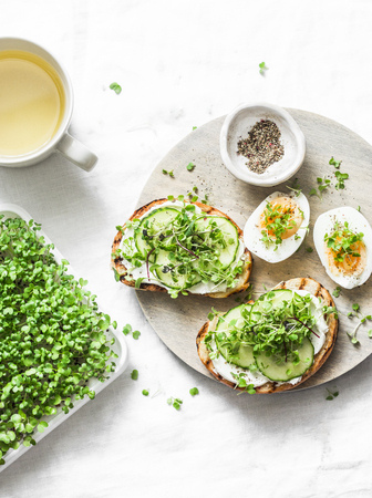 Breakfast, snack, brunch - cream cheese, cucumber, micro greens sandwiches, boiled egg and green tea on a light background, top viewの写真素材