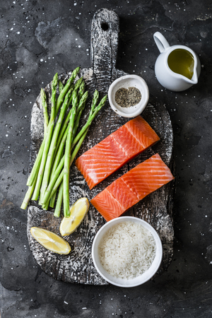 Ingredients for lunch - fresh raw organic salmon, green asparagus and rice on a dark background, top viewの写真素材