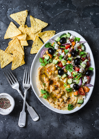 Loaded Greek salad hummus with corn tortilla chips on dark background, top view. Delicious appetizer, tapas in a Mediterranean styleの写真素材