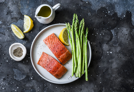 Healthy food ingredients - red fish salmon and fresh green asparagus on a dark background, top viewの写真素材